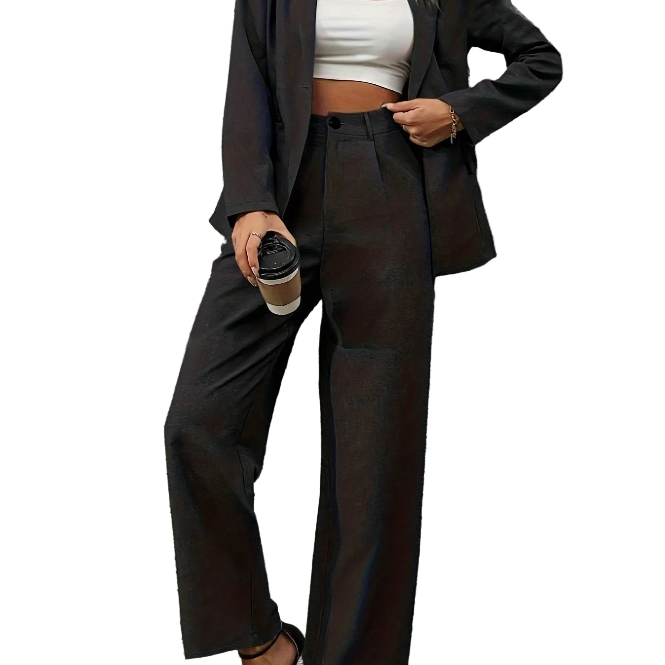 Person wearing a black suit and white crop top against a gray brick wall.