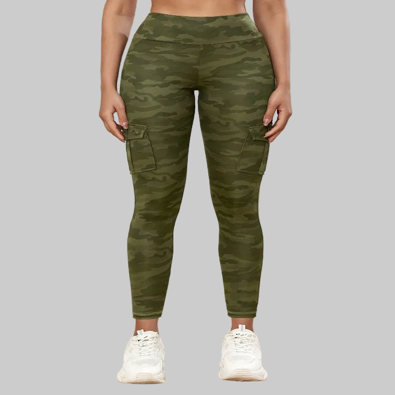 Person wearing green camouflage pants and white sneakers on a wooden floor.