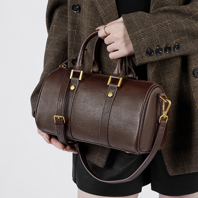A person holding a brown retro portable cowhide crossbody bag with a leather texture and metal buckles.