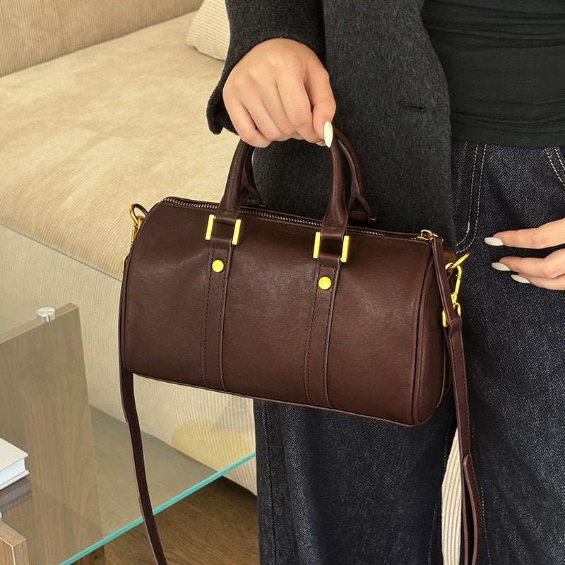 Person holding a brown leather handbag with gold hardware.