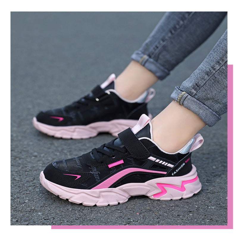 Black and pink children's sneakers worn on a gray pavement.