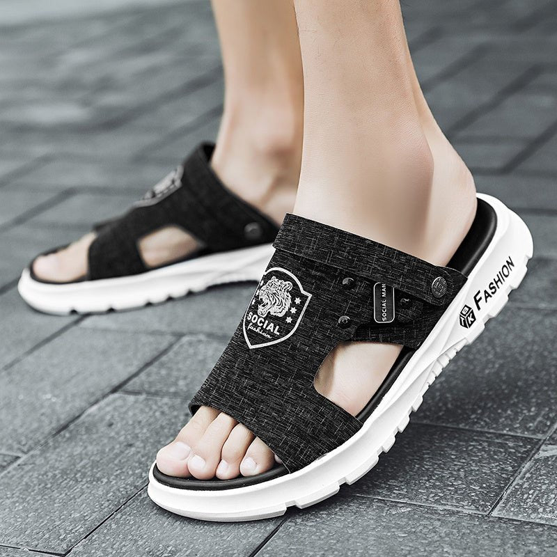 Black sandals with white soles worn on a gray pavement