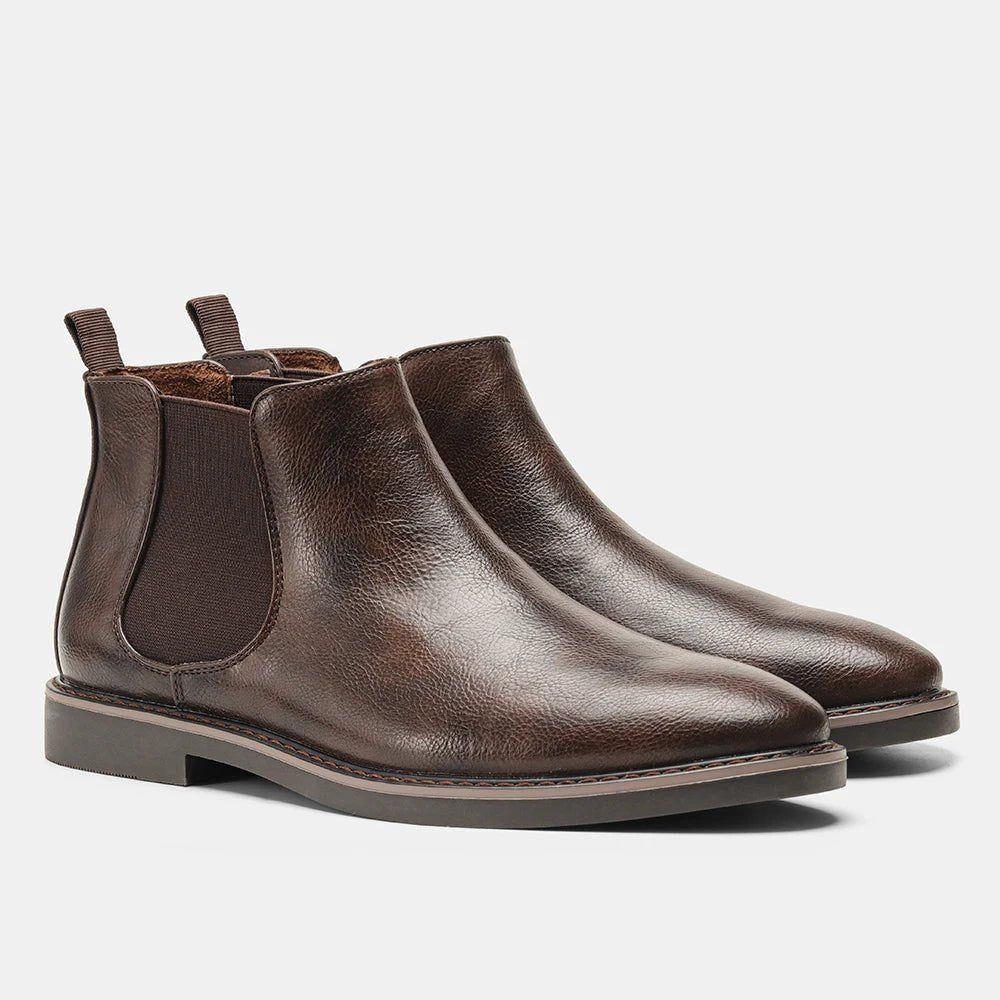 A pair of brown premium leather Chelsea boots with a black rubber sole, displayed in a way that shows the side profile and the boot's interior.