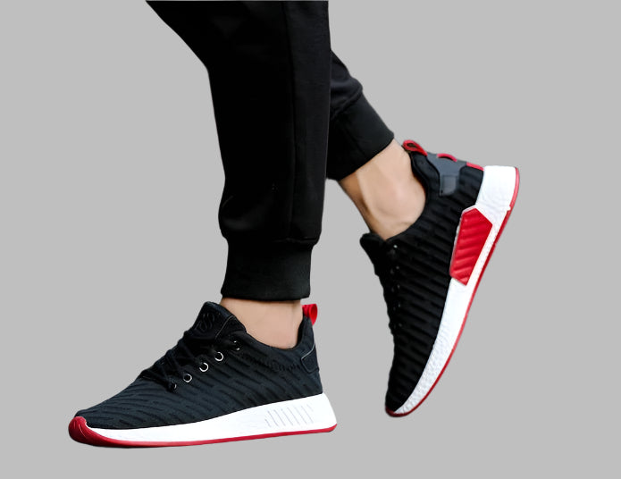 Black and red sneakers worn with black pants on a gray background
