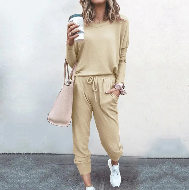 Person wearing a beige tracksuit holding a coffee cup against a plain background