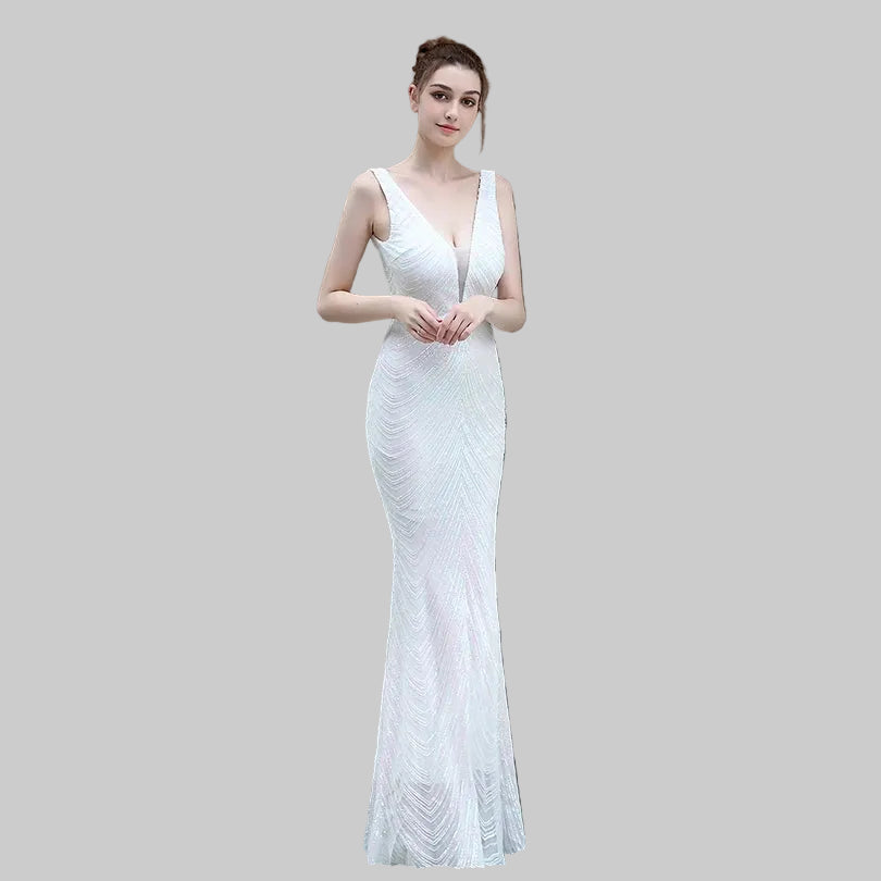 Woman in a white evening gown standing against a green wall.