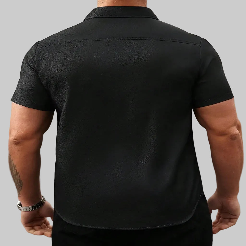 Person wearing a black short-sleeve guayabera shirt with a blurred background