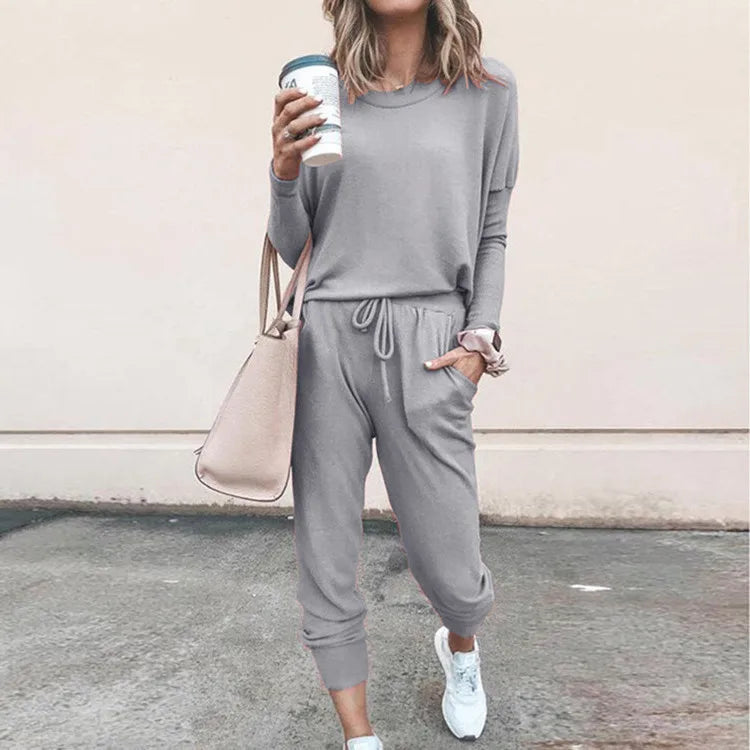 Person wearing a gray tracksuit holding a coffee cup against a plain background