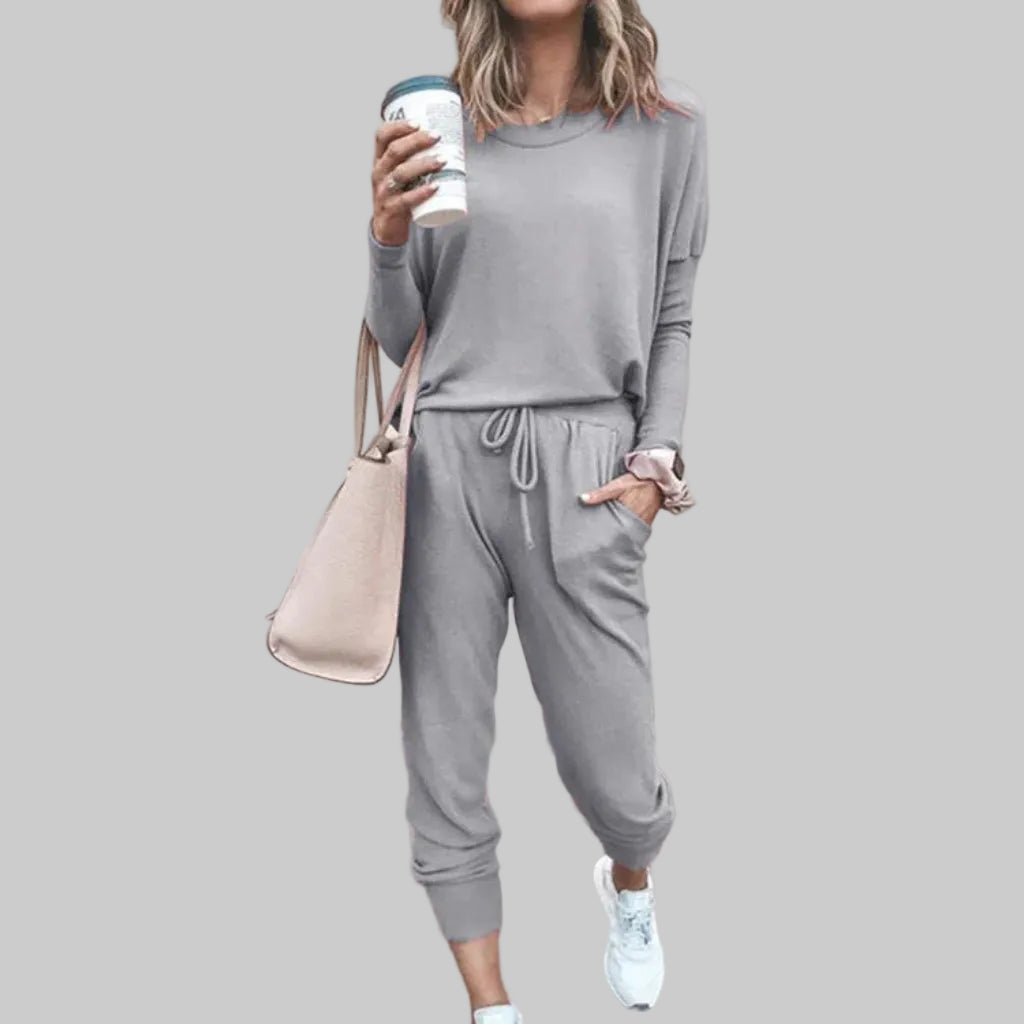 Person wearing a gray tracksuit holding a coffee cup against a plain background