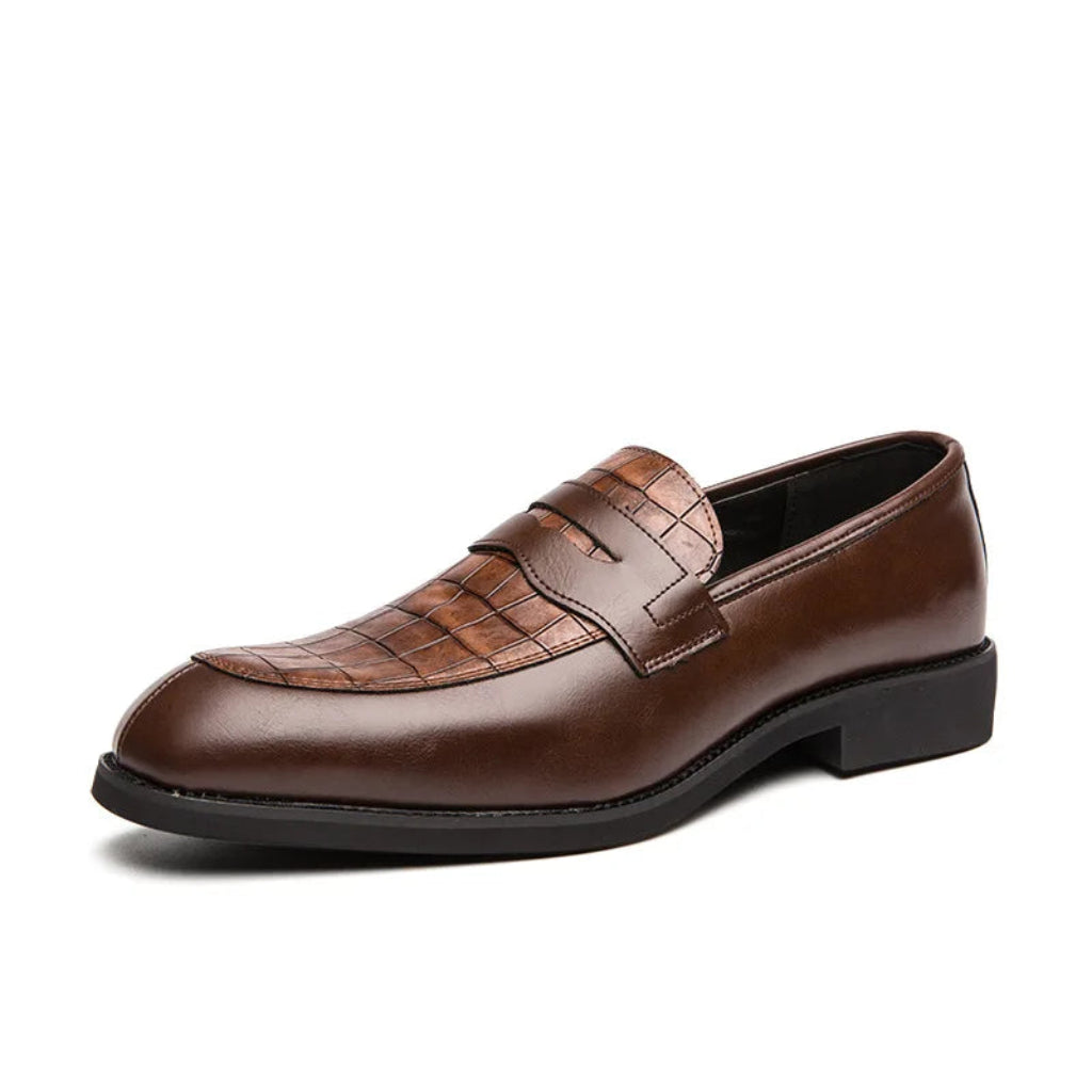 A man's foot wearing a brown crocodile-patterned leather shoe with a buckle strap, alongside a wooden floor and a wristwatch.