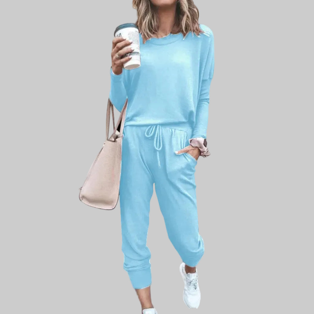 Woman wearing a light blue tracksuit holding a coffee cup against a plain background