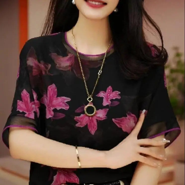 Woman wearing a black floral blouse with a gold necklace and jewelry.