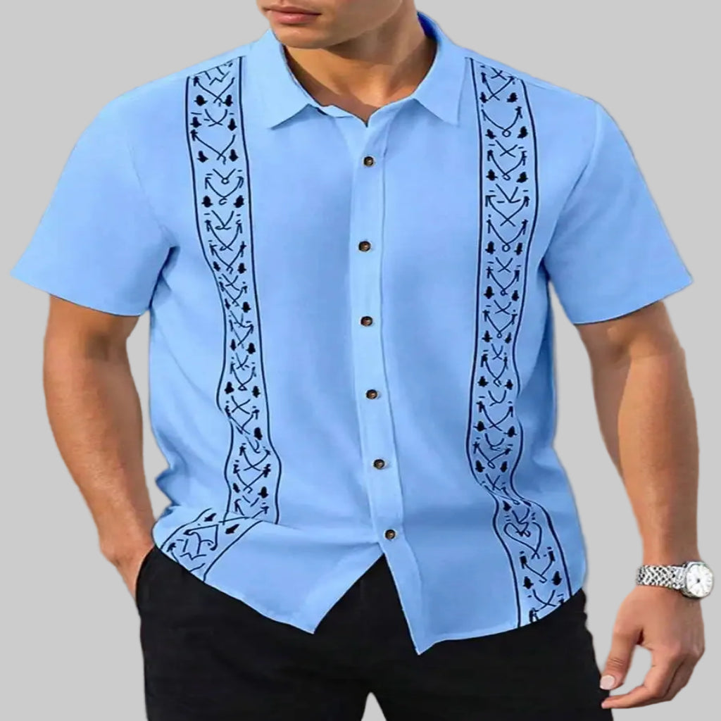 Light blue short-sleeve guayabera shirt with black embroidery on a beige background