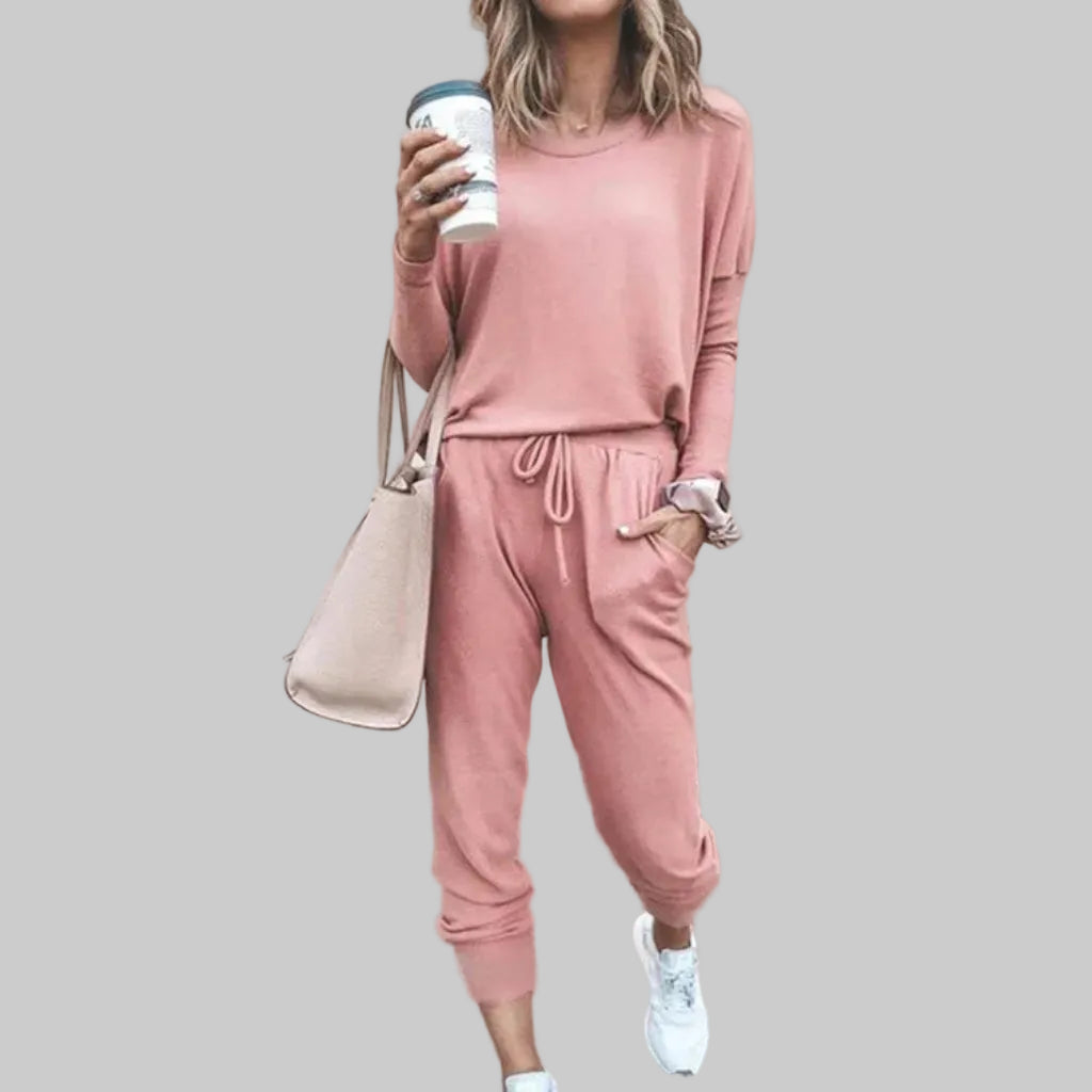 Person wearing a pink tracksuit holding a coffee cup against a plain background