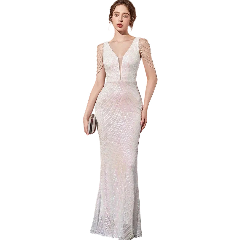 Woman in a white evening gown standing in front of a brown curtain.