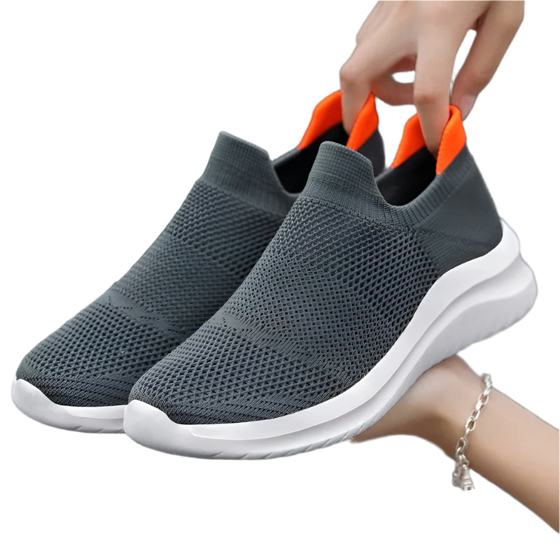 Gray slip-on sneakers with orange accents held by a hand on a white background