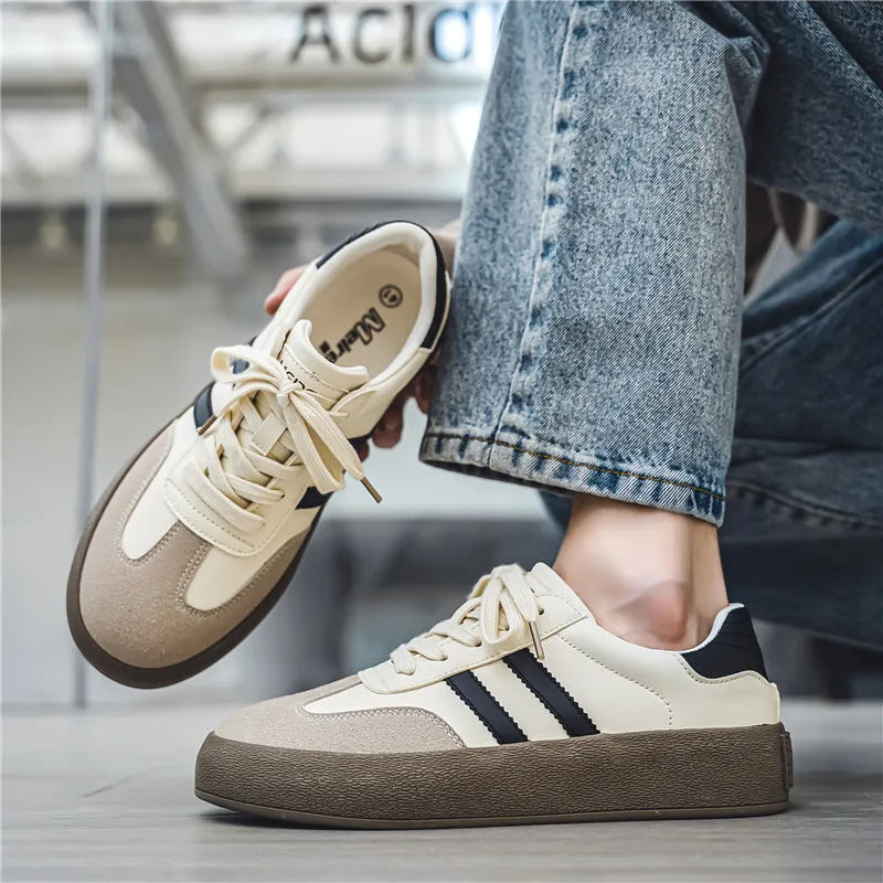 Pair of beige and brown sneakers with a person wearing them, holding one shoe.