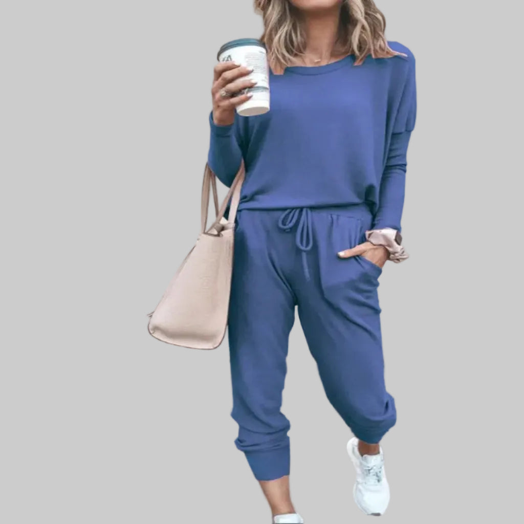 Person wearing a blue outfit holding a coffee cup against a beige wall.