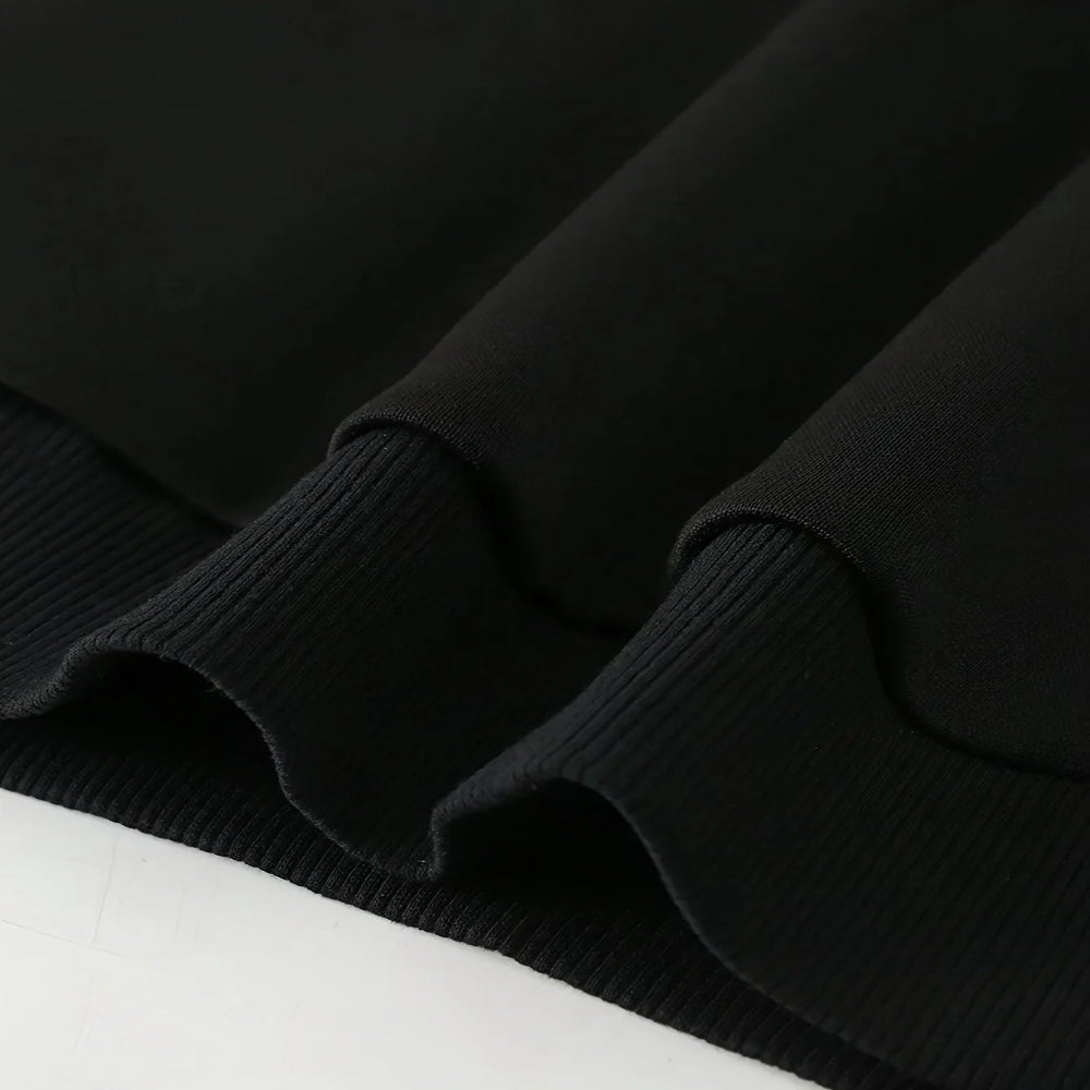 Close-up of a black ribbed knit garment, showing the texture and folded ruffled edge against a white background.