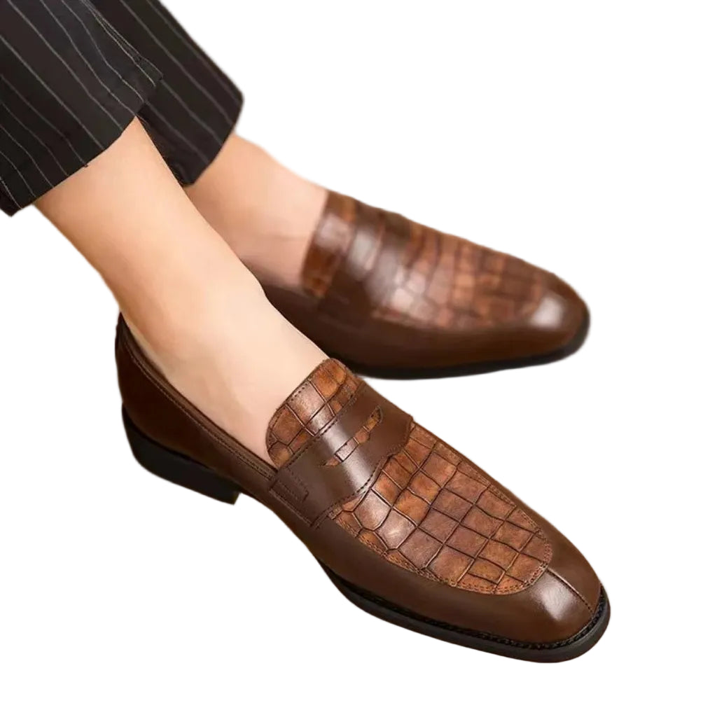 Brown leather shoes with textured pattern worn by a person on a wooden floor.