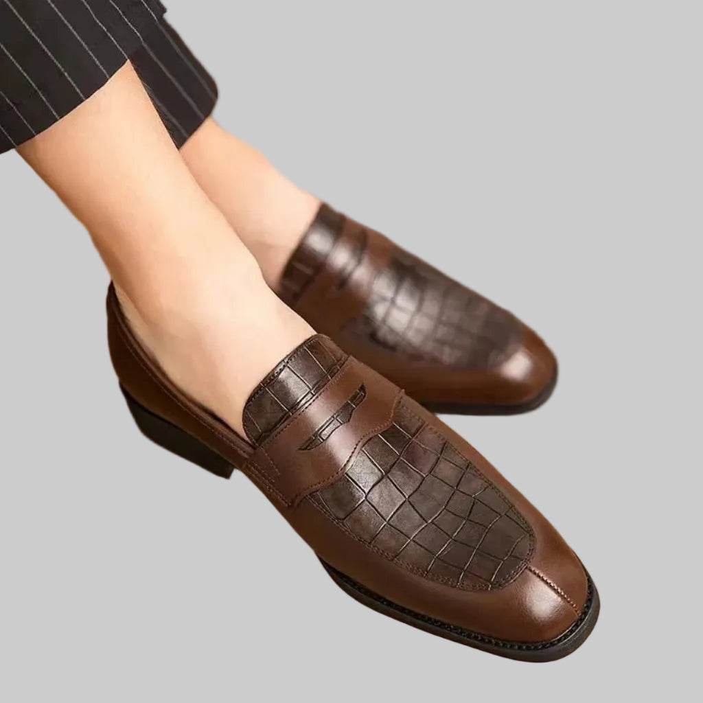 Brown loafers worn by a person on a wooden floor