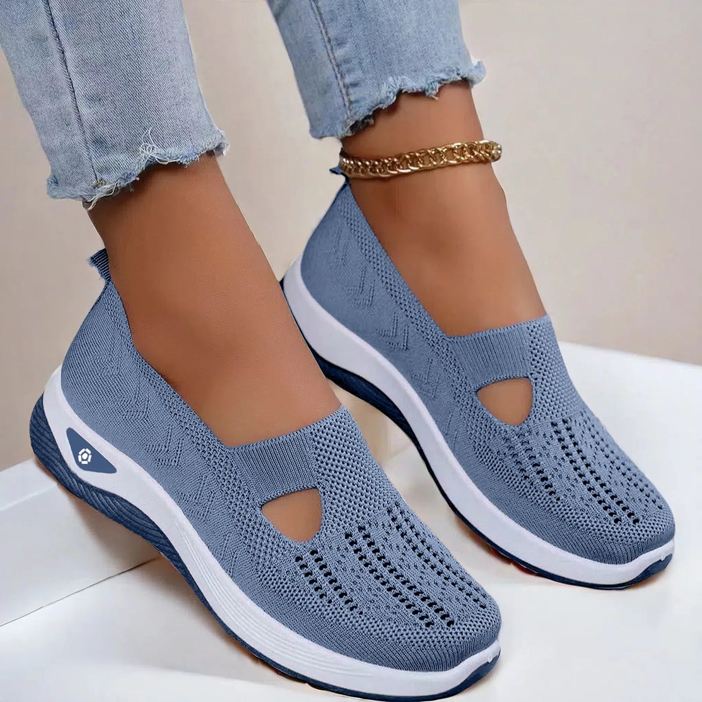 A pair of light blue women's casual walking shoes with a slip-on design, shown being worn by a person standing on a white surface. The shoes feature a breathable knitted mesh upper and a lightweight sole with anti-slip grip.