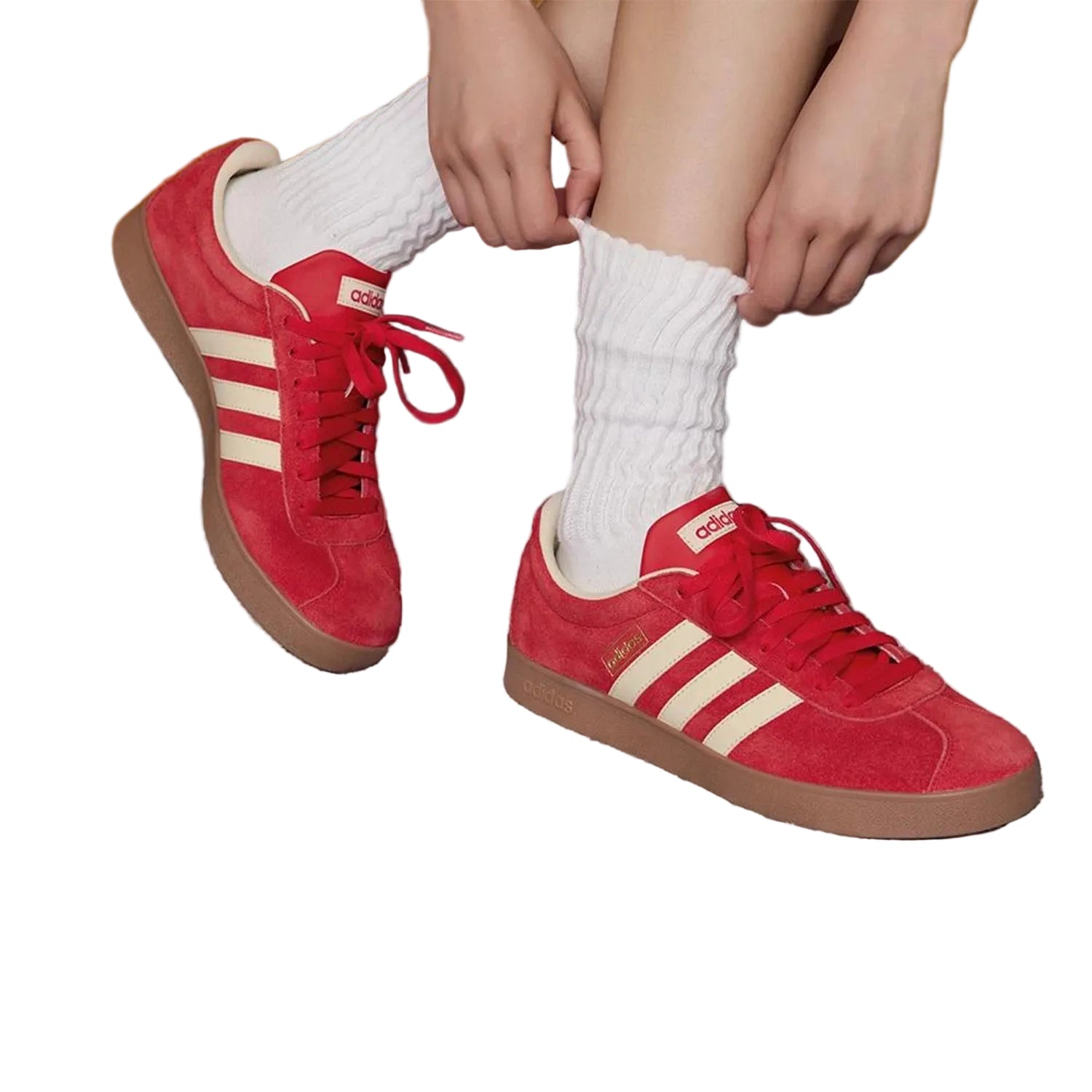 Red Adidas sneakers with white stripes worn by a person on a gray floor.