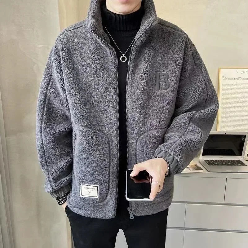 Person wearing a gray fleece jacket with a brand logo, holding a phone indoors.