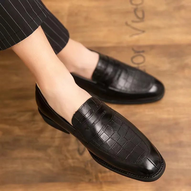 Black leather loafers worn by a person on a wooden floor.