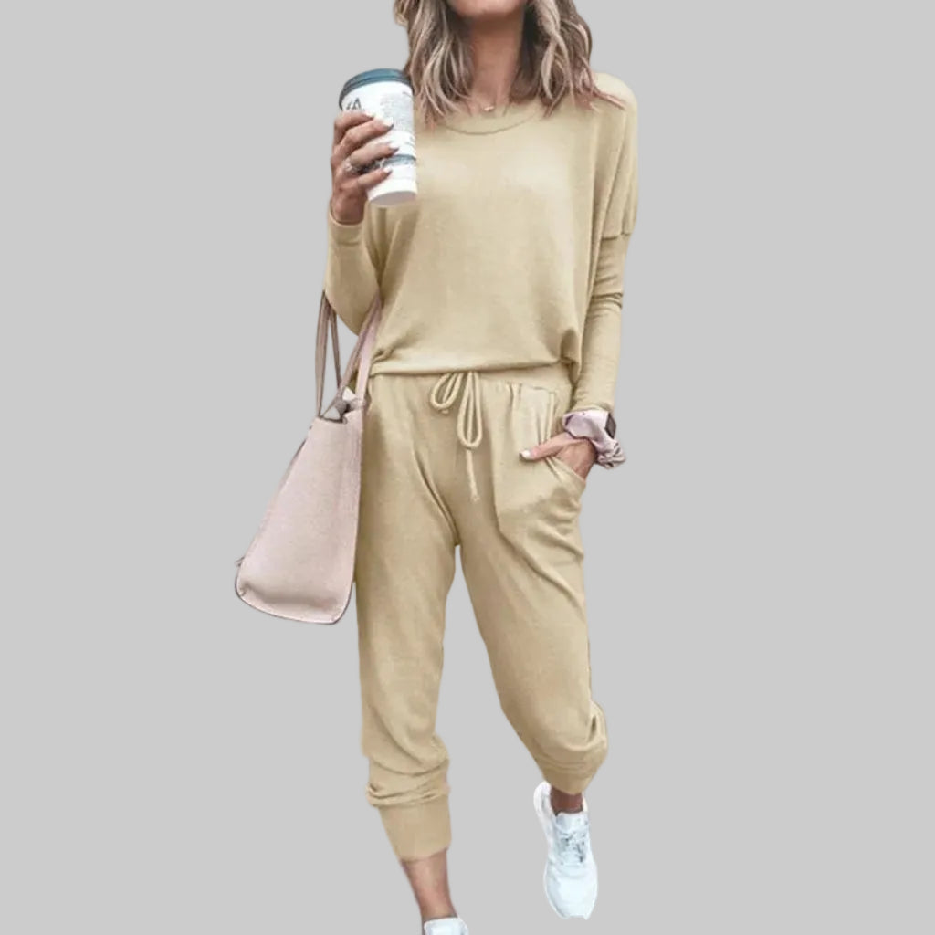 Person wearing a beige tracksuit holding a coffee cup against a plain background