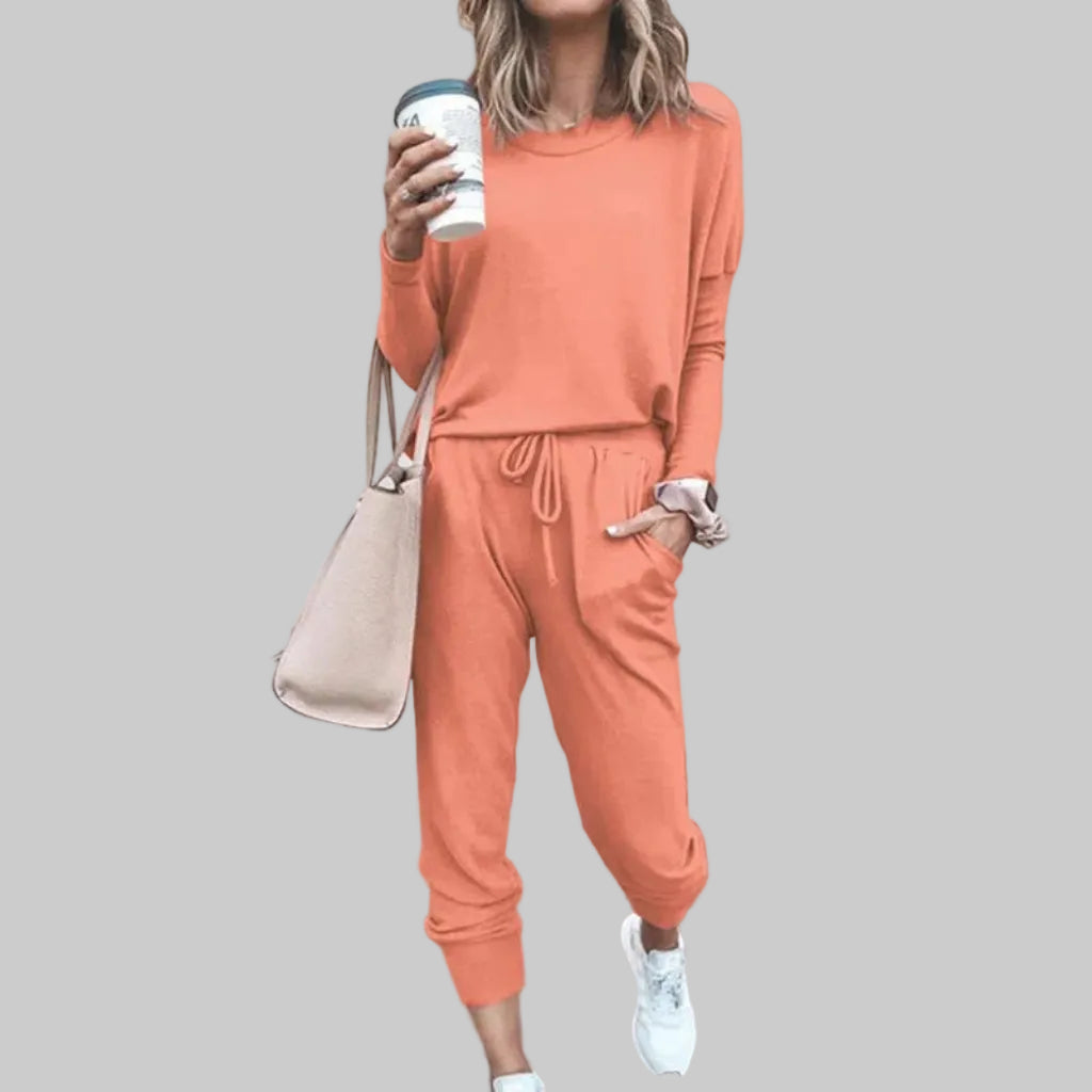 Woman wearing a peach tracksuit holding a coffee cup against a plain background