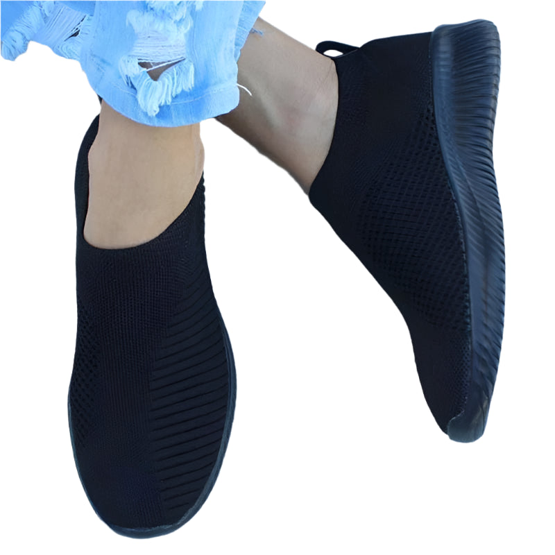 Black slip-on shoes worn by a person with blue gloves on a white background
