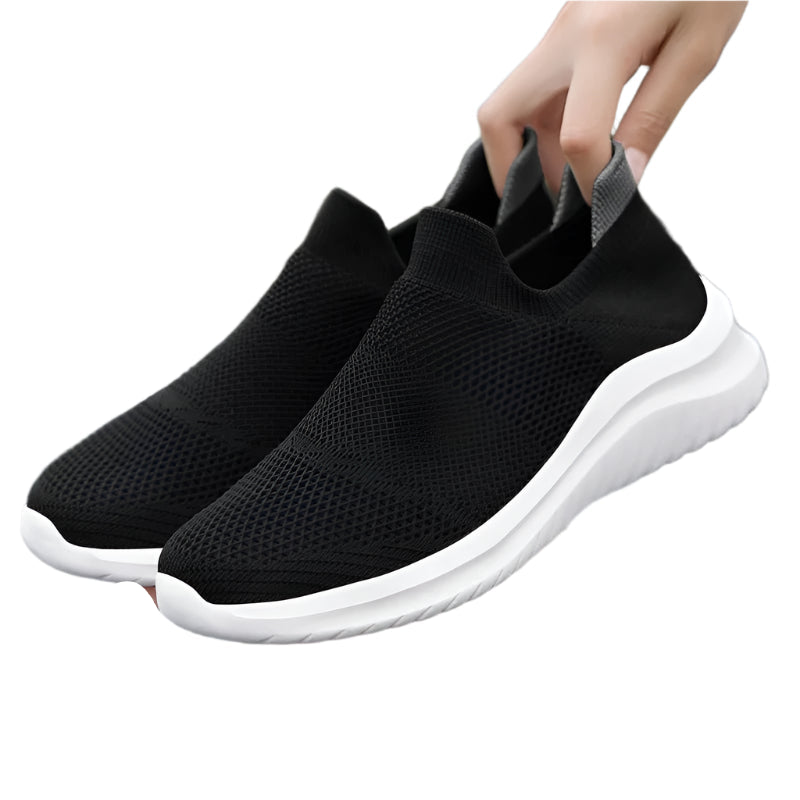 Black slip-on sneakers with white soles on a white background
