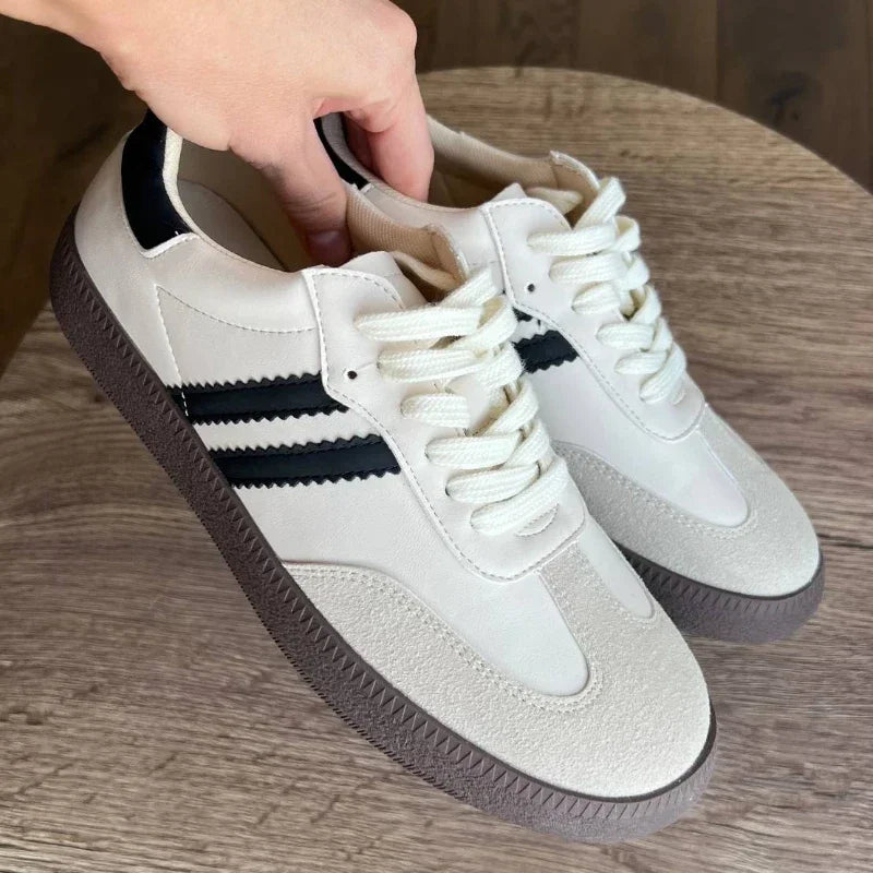 White sneakers with black stripes on a wooden surface