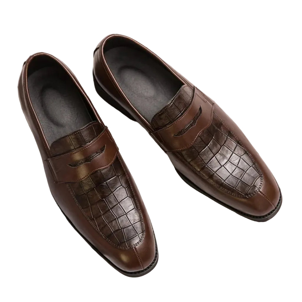 A man's foot wearing a brown crocodile-patterned leather shoe with a buckle strap, alongside a wooden floor and a wristwatch.