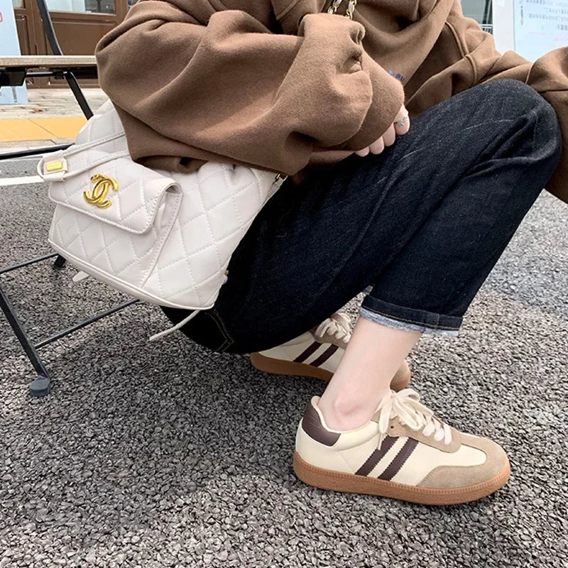 Person wearing a brown hoodie and dark jeans, sitting on a chair with a white Chanel bag.