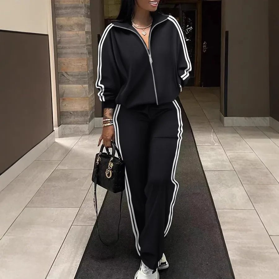 Person wearing a black tracksuit with white stripes, holding a black handbag, standing on a tiled floor.