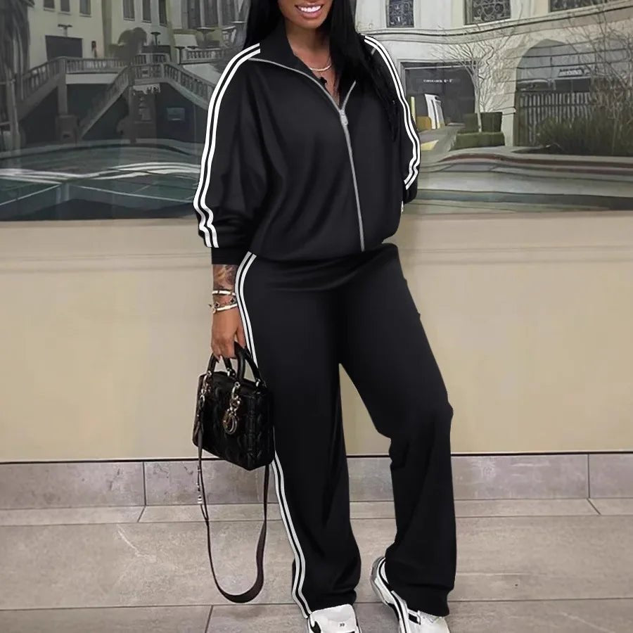 Person wearing a black tracksuit with white stripes, holding a black handbag indoors.