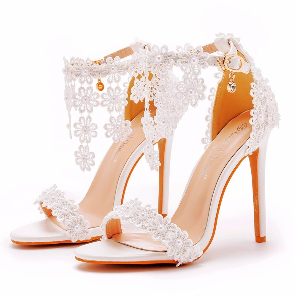 Elegant high-heeled sandals with white lace and floral decorations on a white background.