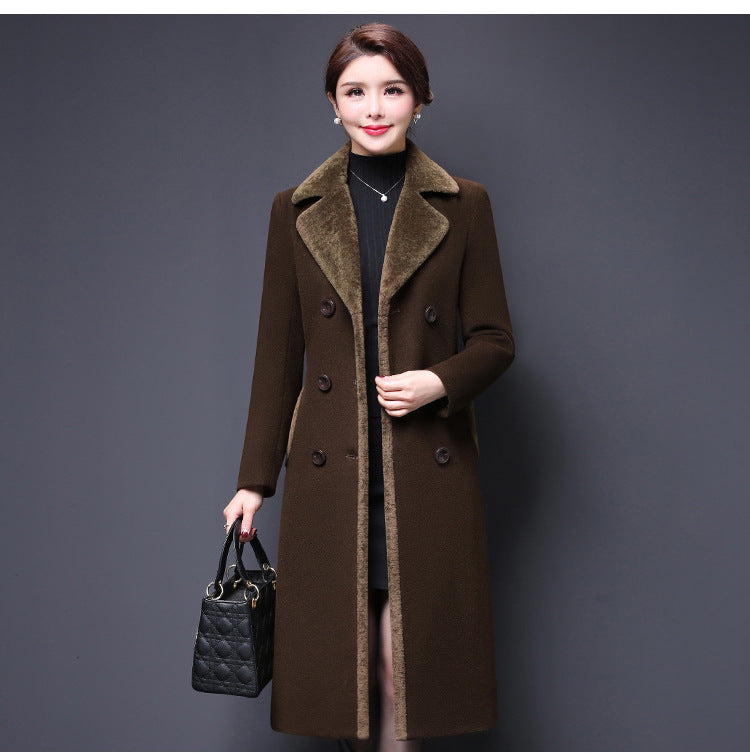 Woman wearing a brown coat holding a black handbag against a gray background