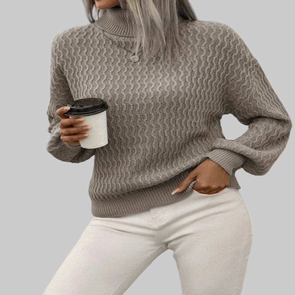 Person wearing a gray knitted sweater holding a coffee cup indoors.