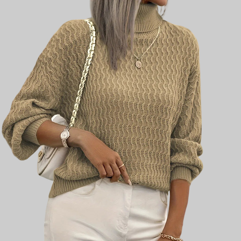 Person wearing a beige knitted sweater with a neutral background