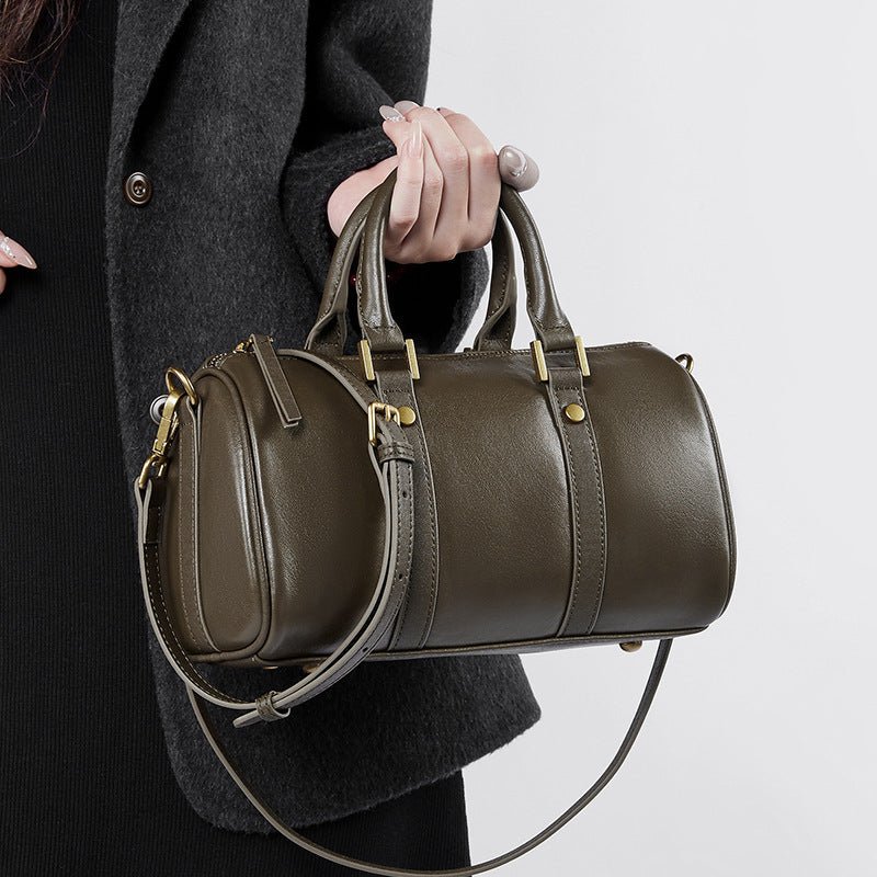 Person holding a green leather duffel bag against a neutral background.